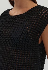 Mustat virkattu toppi, jossa on ruudukko kuvio, leveä kaula-aukko ja hihat. Tekstuurissa on avoin neule, joka paljastaa ihon alla.