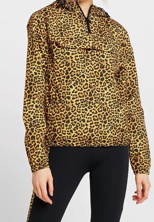 Femme portant un pull à manches longues imprimé léopard avec une fermeture éclair à l'avant et un pantalon noir ajusté.