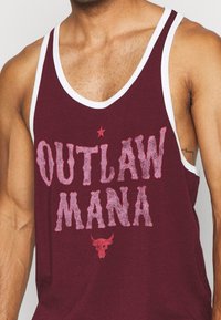 Bordowy top na ramiączkach z białymi wykończeniami, z napisem "OUTLAW MANA" w pogrubionej, postarzanej czcionce i małą grafiką czaszki byka poniżej.