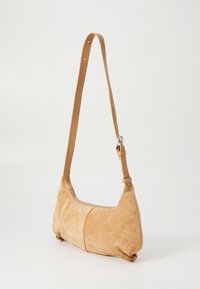 Bolso de hombro de gamuza color crema con una sola correa ajustable, forma redondeada, cierre de cremallera y acentos decorativos en la correa.