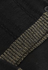 Svart stickat tyg med en texturerad design, som har en guld- och svart ribbad accent samt en rund svart knappdetalj.