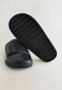 Sorte sandaler med en tekstureret gummisål, åben design og justerbar rem. Glat syntetisk overdel med et subtilt mønster.