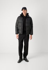 Svart puffjakke med quiltet design, sidelommer; lagt over en svart hettegenser. Svart bukser og sko fullfører stilen.
