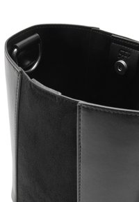 Czarna torebka łącząca gładką i fakturowaną skórę, o cylindrycznym kształcie, z delikatnym przeszyciem i metalowym pierścieniem jako ozdobą.