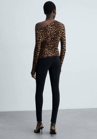 Halenka s leopardím vzorem, s dlouhým rukávem a asymetrickým výstřihem, spárovaná s černými přiléhavými legínami a sandály na vysokém podpatku se straps.
