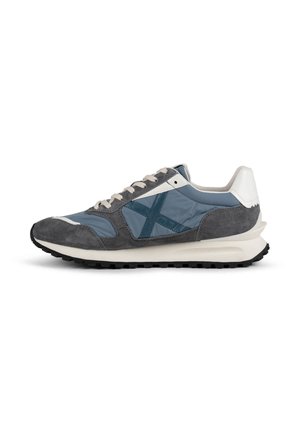 Zapatilla de running con paneles azules y grises, talón y cordones blancos, y suela negra estriada, vista de lado sobre fondo blanco.