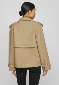 Kamelfärgad ullblandad kappa med bred krage, dubbelknäppt design och bälte vid ärmsluten. Har en lagerpälsig detalj bak och en strukturerad passform.