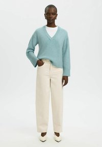 Light blue knitted sweater with a V-neck, long sleeves, and ribbed hem, paired with beige wide-leg pants and white pointed-toe heels.