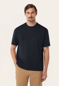 Middendonk blauw T-shirt met korte mouwen en een ronde hals, gemaakt van een gladde stof, ontspannen pasvorm, gedragen met kaki broek, met subtiele stiksels.