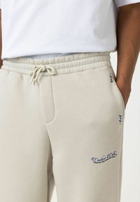 Lichtgrijze sweatpants van een zachte katoenmix, met een tailleband met trekkoord, zijzakken en blauwe geborduurde accenten.