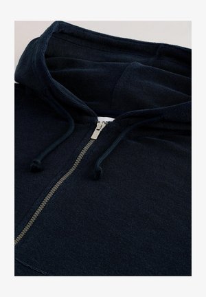 Navy blue zip-up collegepaita, valmistettu pehmeästä kankaasta. Siinä on huppu, hopeinen vetoketju ja nyörit. Teksturoitu ulkonäkö ja rento muotoilu.