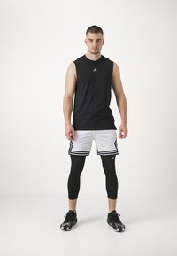 Débardeur sans manches noir, short en maille blanche avec accents noirs, legging de compression noir et chaussures de sport noires. Logo Jordan en évidence.