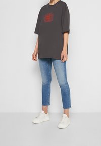 Tmavě šedé oversized tričko s červeným grafickým designem na hrudi, doplněné světle modrými skinny džíny a bílými teniskami.