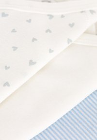 Tessuto bianco con piccoli cuori grigi stampati su uno strato, sovrapposto a un tessuto a righe blu chiaro e bianco sottostante. Texture morbida.