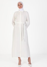 Long white dress with a button-down front, collar, and belted waist. Made of lightweight fabric with long sleeves, featuring a smooth texture.