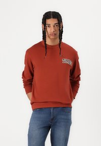 Roestkleurige sweatshirt met ronde hals en ribgebreide mouwen. Beschikt over een klein "TIMBS"-logo op de linkerkant van de borst. G combineren met blauwe spijkerbroek.