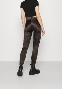 Leggings en satin marron avec des détails froncés, taille haute et coupe ajustée, associées à des bottines noires.