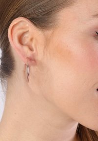 Roségoldene Creole, kreisförmig, glatte Oberfläche, leichtes Metall, hängend am Ohrläppchen, mit polierter Oberfläche.