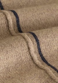 Strickstoff in Beige mit strukturierter Oberfläche, der dunkelblaue horizontale Streifen aufweist. Eine Nahaufnahme hebt das Gewebe und die Details hervor.