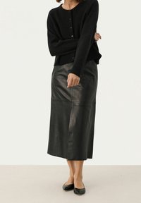 Svart stickad cardigan med knappstängning, ihopparad med en lång svart läderkjol med en slät yta och rak skärning. Svarta ballerinas fulländar looken.