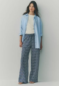 Ljusblå button-up skjorta över en vit t-shirt, ihop med lösa, marint mönstrade byxor med dragsko i midjan och vida ben.