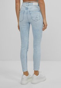 Ljust blå smala jeans med en blekt textur, som har hög midja, två bakfickor och slitna detaljer på yttre bensöm.