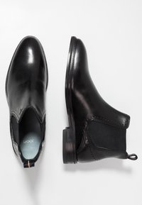 Botas de tobillo de cuero negro con paneles laterales elásticos, puntera redondeada y acentos texturizados. Incluyen una pestaña para tirar y un acabado suave y brillante.
