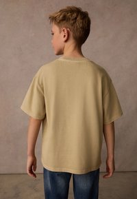 Beige kortärmad t-shirt med rund halsringning och lös passform, tillverkad av ribbat tyg; bärs tillsammans med blå jeans.