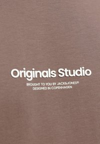 Camiseta de algodón marrón con texto impreso en blanco: "Originals Studio", "Traído a ti por JACK&JONES" y "Diseñado en Copenhague."