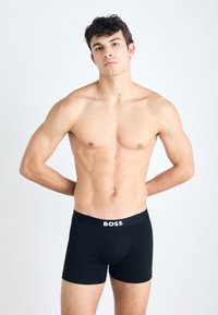 Black boxer shorts with a soft, elastic waistband featuring the text "BOSS" in white. The fabric appears smooth and stretchy.