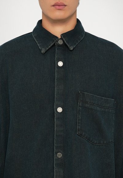 Mørk denim skjorte med knapp foran, klassisk krage, sølvknapper og en brystlomme. Tøyet har et mykt, teksturert utseende.