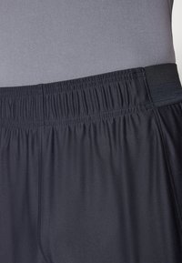 Sorte atletiske shorts med elastisk talje, glat tekstur og subtil glans, parret med en grå tætsiddende top.