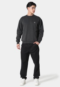 Felpa grigio scuro in misto cotone, con polsini e orlo a costine, tasche laterali e un dettaglio logo discreto. Abbinata a pantaloni neri e sneaker bianche.