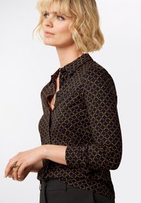 Camicia nera con bottoni e motivo geometrico arancione e giallo, maniche lunghe con polsini, dotata di colletto classico e design aderente.