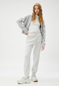 Sudadera gris claro y pantalones de chándal a juego. Tejido suave y texturizado con puños y cinturilla elásticos. Zapatillas blancas con acentos beige.