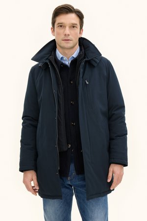 Navy blue padded coat with a high collar, zip and button closures, side pockets, worn over a dark sweater and light shirt, casual fit.
