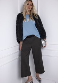 Jasnoniebieska bluza z napisem "PARIS", czarne teksturowane szerokie spodnie, czarna kurtka z sztucznego futra, srebrne dodatki oraz metaliczne sandały.