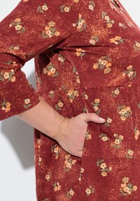Bordeauxrotes Kleid mit einem strukturierten Blumenmuster in Orange und Grün, mit Dreiviertelärmeln und einer Seitentasche.