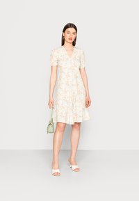 Vestido floral com decote em V, mangas bufantes e saia rodada em cores pastel; combinado com mules brancas de salto e uma bolsa verde menta.