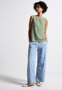 Green sleeveless top with pleats, paired with light blue wide-leg jeans and cream flat shoes. Smooth fabric with clean design lines.