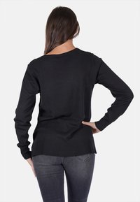 Maglione nero a maglia con maniche lunghe, con polsini e orlo a coste. La parte posteriore ha una lunghezza leggermente maggiore con un collo a giro classico.