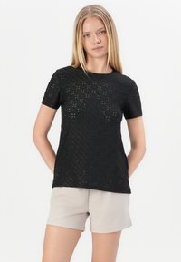 Zwart t-shirt met korte mouwen, gemaakt van textuurstof met een laser gesneden patroon, met een ronde hals. Draagt met lichtbeige korte broek.