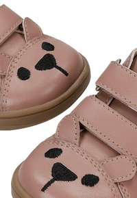 Chaussures roses pour tout-petits avec des brides Velcro et des visages et oreilles d'ours noirs cousus sur les orteils.