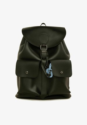 Mochila de imitación cuero negro con una tapa redonda, hebilla plateada, dos bolsillos frontales y una etiqueta azul. Textura suave con detalles de diseño mínimos.