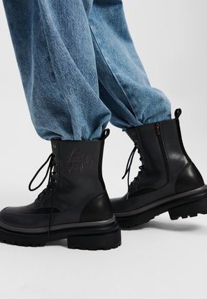 Black leather combat boots with round toes, ribbed rubber soles, lace-up front, and a side zipper. Features embossed lettering on the shaft.