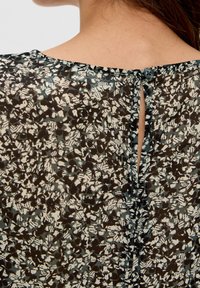Schwarze und cremefarbene gemusterte Bluse mit Rückseite, die über ein Schlüssellochdetail und eine Knopfverschluss verfügt, aus leichtem Stoff mit strukturierter Oberfläche.