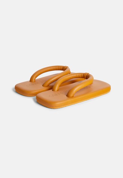 Oranje rubberen slippers met dikke, ronde banden en een gestructureerde voetbed. Voorzien van een platte, rechthoekige zool en minimale branding.