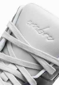 Baskets en cuir blanc avec des accents gris, dotées de lacets plats, d'une marque en relief et d'une zone de pointe texturée, mettant en avant un design épuré et minimaliste.