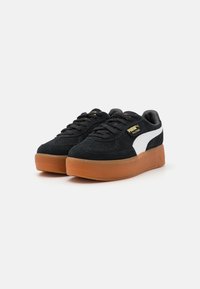 Sneakers negri din suede cu logo și șireturi albe, având o talpă din gumă cu platformă și un design cu vârf rotunjit. Accente aurii pe detaliile de branding.