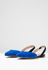 Blaue Wildleder Slingback-Ballerinas mit einem spitzen Zehendesign, kontrastierendem schwarzen Rücken und einer glatten beigen Innensohle. Flache Gummisohle.